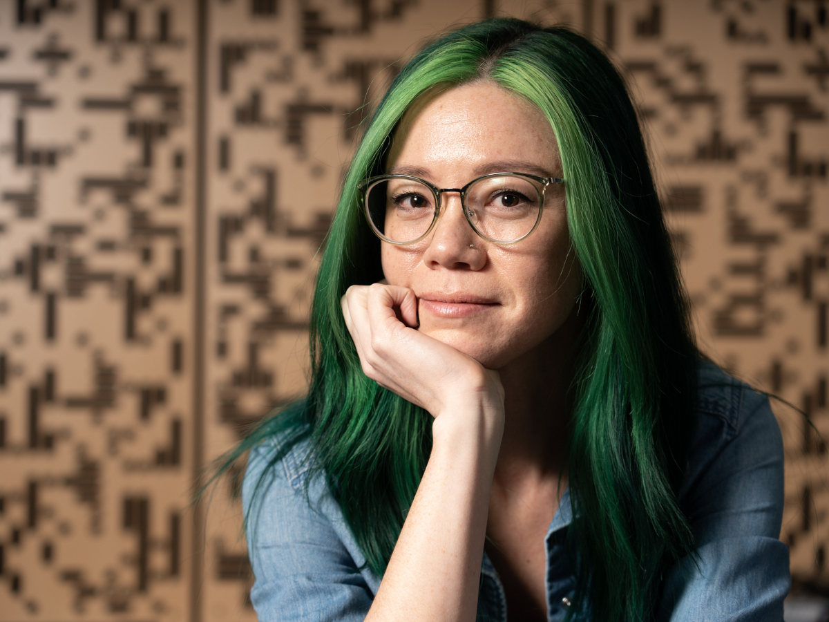 a photo of Alex King, with long green hair, looking at the camera and smiling slightly